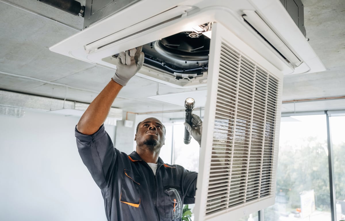 Repair technician working on ventilation inside a modern office